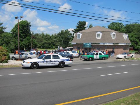 1991 Ford LTD Crown Victoria - white police traffic Crown Victoria parked along the road beside a brick building, with a crowd and other cruisers behind.