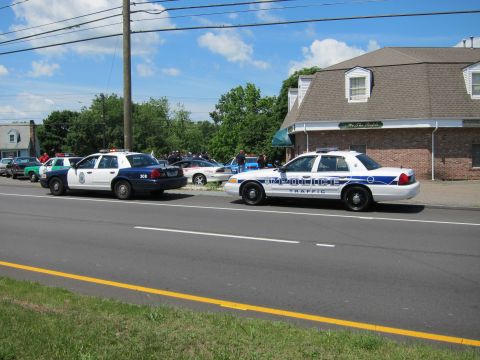 1991 Ford LTD Crown Victoria - Two white police traffic cruisers parked along a roadway near a brick building, with people gathered in the background.