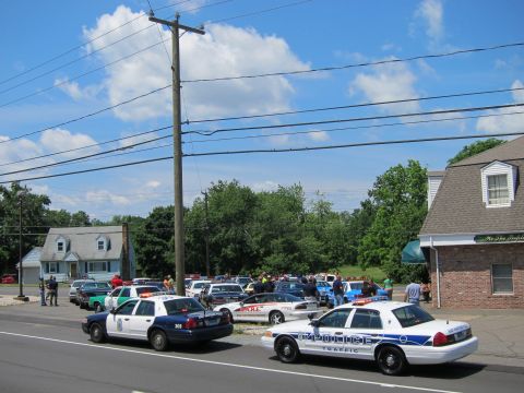 1991 Ford LTD Crown Victoria - gathering of police cruisers and other cars filling a lot beside a brick building under a partly cloudy sky.