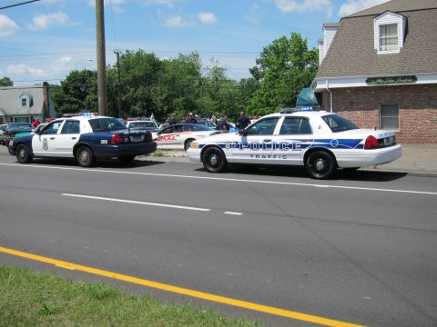 1991 Ford LTD Crown Victoria - white police traffic Crown Victoria and a green-and-white cruiser parked along the road beside a brick building.