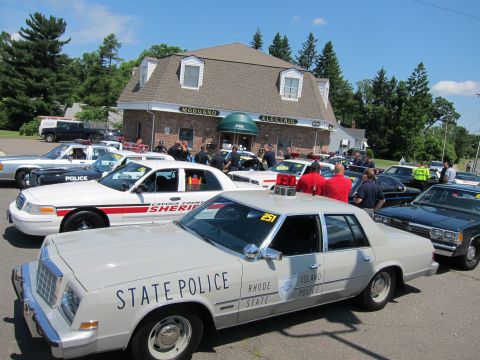 1991 Ford LTD Crown Victoria - white Rhode Island State Police sedan marked 251 parked among other police cars in a crowded lot by a brick building.