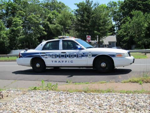 1991 Ford LTD Crown Victoria - side profile of an East Hartford Police Traffic Crown Victoria parked by a tree-lined roadside on gravel.