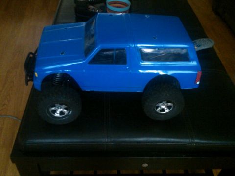1986 Ford Bronco - Blue remote control car body, possibly a Ford Bronco replica, sits on a dark upholstered surface.