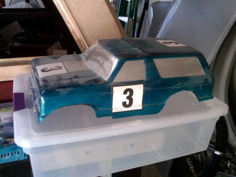1986 Ford Bronco - Blue RC car body with racing numbers '3' on doors and hood sits on a plastic container.