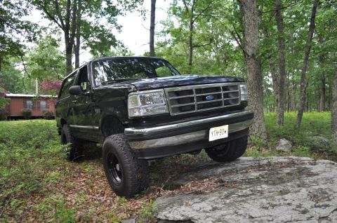 1995 Ford Bronco - A black Ford Bronco is shown navigating a rocky terrain in a wooded area.