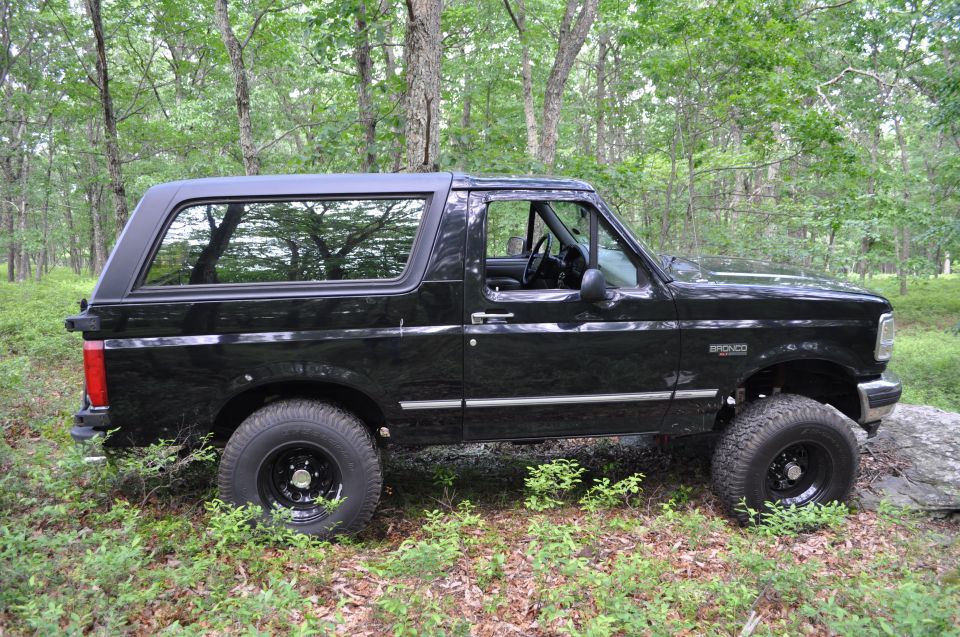 Black Ford Bronco SUV parked on a wooded trail, side view
