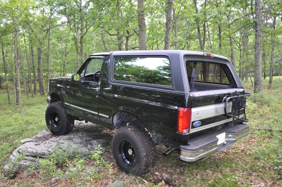 1995 Ford Bronco parked on rocks, rear 3/4 view, forest background