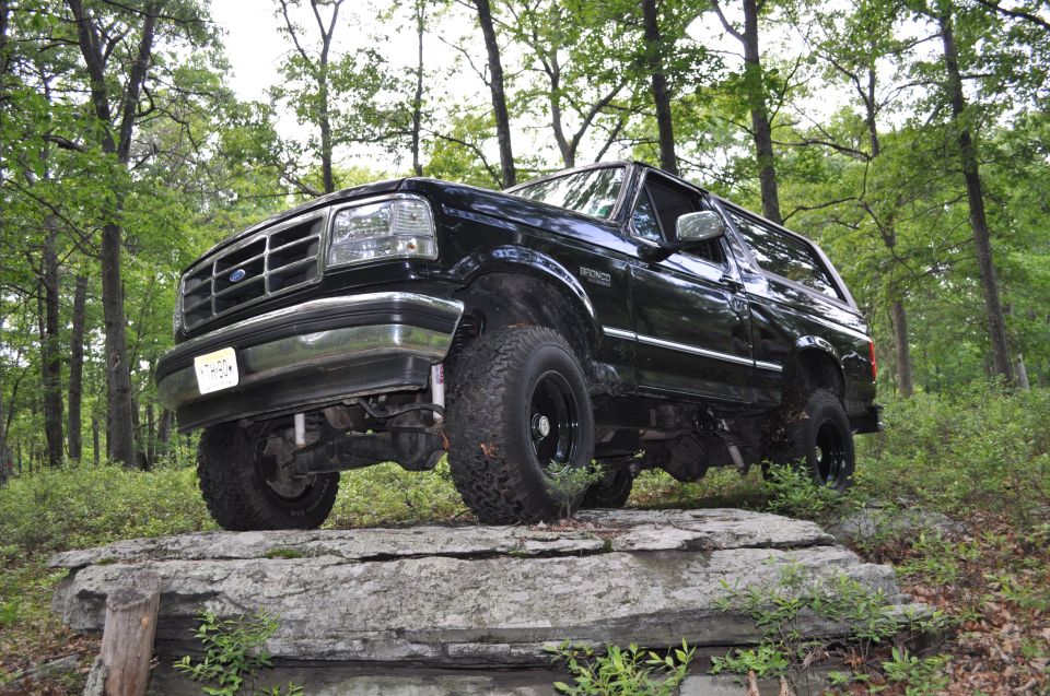 Black Ford Bronco on rocks in woods. License plate visible