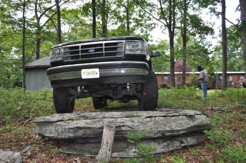 1995 Ford Bronco - A black Ford Bronco is positioned on large rocks in a wooded area, with a person standing in the background.