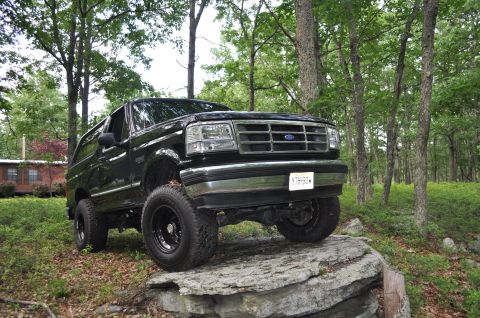 1995 Ford Bronco - This black 1995 Ford Bronco is positioned on large rocks in a wooded area.