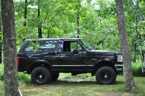 1995 Ford Bronco - A black 1995 Ford Bronco is parked on a grassy area surrounded by trees.