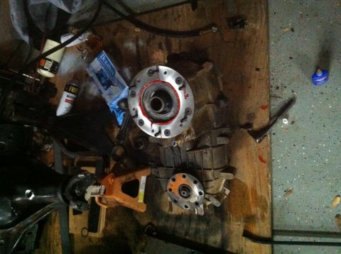 1996 Ford Bronco - A transfer case sits on a plywood workbench mid-rebuild, its freshly machined output housing sealed with red RTV around the bolt flange and…