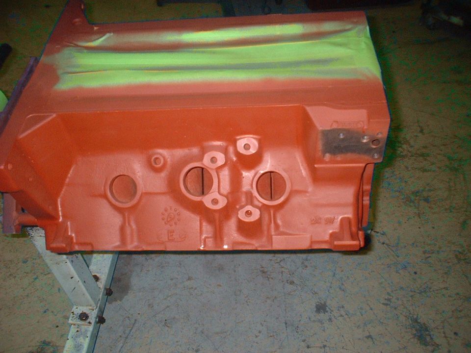 Orange engine block with green masking tape on top. It's sitting on a metal stand