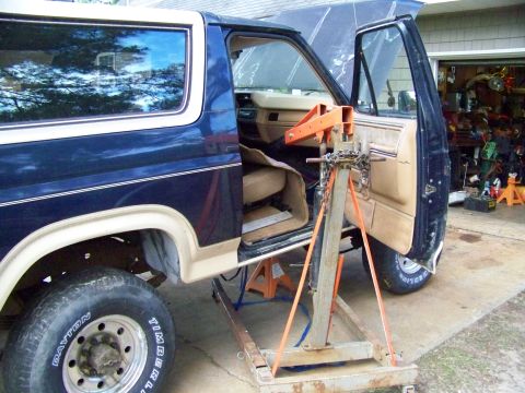 1985 Ford Bronco - A blue and tan Ford Bronco is parked in a garage with its doors open and an engine hoist inside.