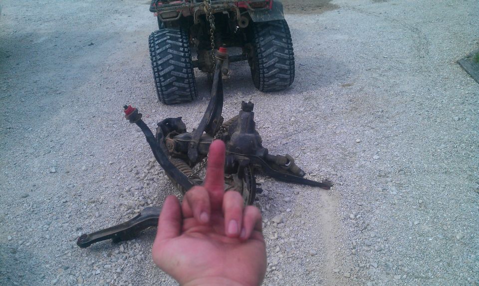 Disassembled suspension components on gravel with an ATV in the background