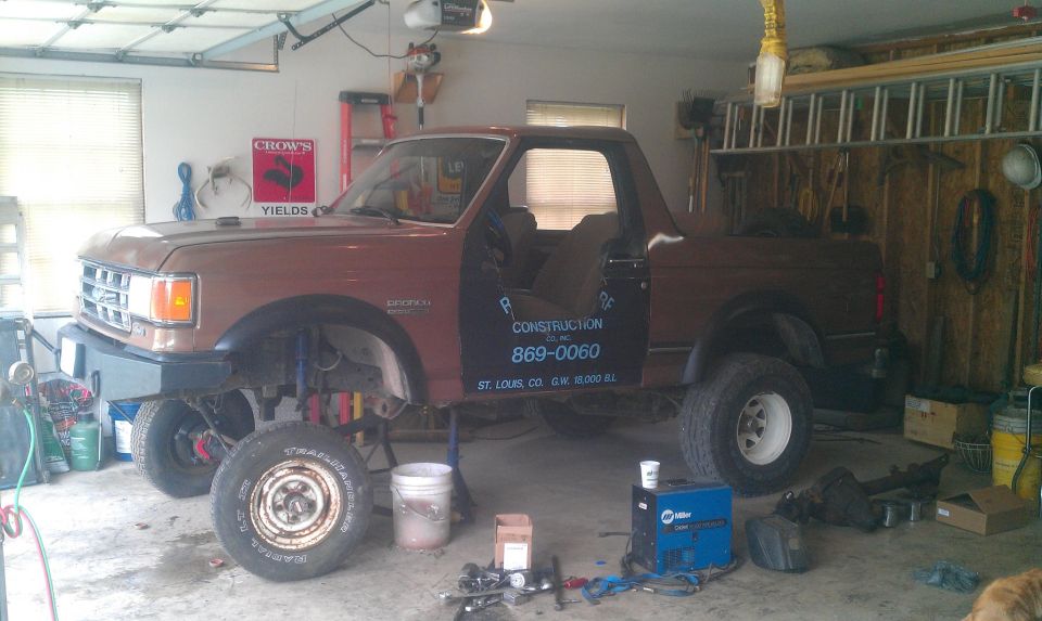 1987 Ford Bronco in a garage, doors open, showing construction company text on the driver's door