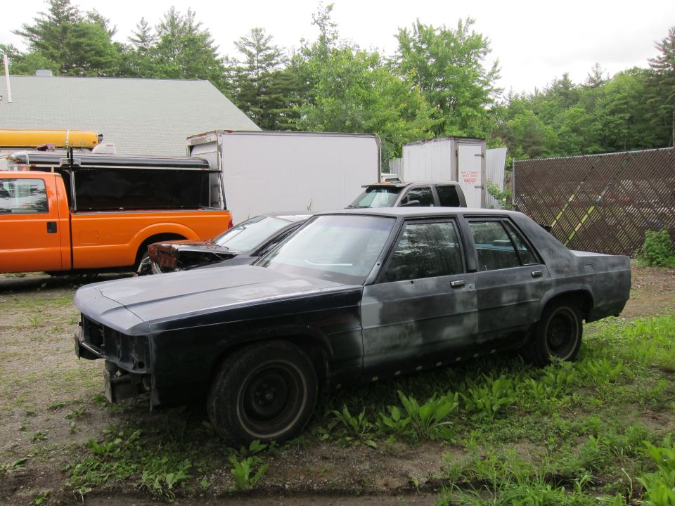 Side view of a black sedan with primer patches, parked outdoors