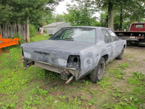 1991 Ford LTD Crown Victoria - A primer-finished sedan sits in a grassy area, awaiting restoration, with a tow truck in the background.