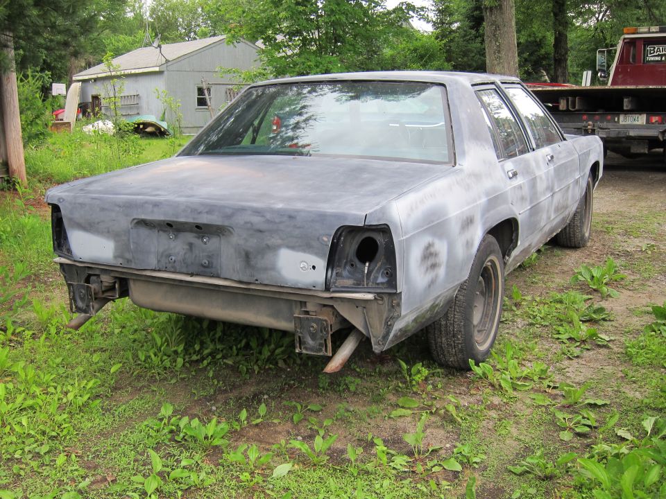 Rear view of a primer-covered sedan with missing taillights and exhaust pipes