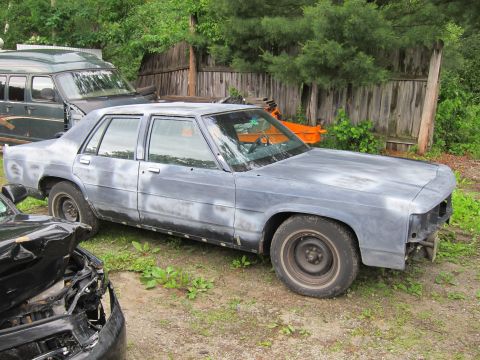1991 Ford LTD Crown Victoria - A sedan, possibly a Ford Crown Victoria, sits in primer next to a damaged car and a van.