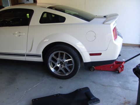 2007 Ford Mustang - Rear quarter view of a white 2007 Ford Mustang, racing stripes and a red hydraulic jack supporting the rear.