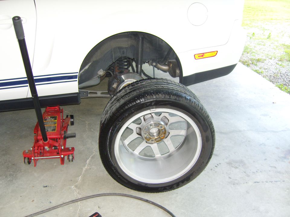 White Ford Mustang with blue racing stripes, jacked up with rear wheel removed