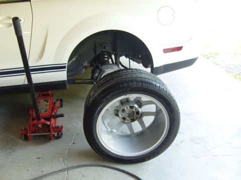 2007 Ford Mustang - A white 2007 Ford Mustang is shown with its rear wheel removed and a jack positioned nearby.