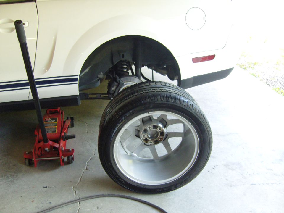 White 2007 Ford Mustang side view with racing stripes, jack, and removed wheel