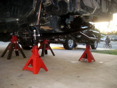 1996 Ford Bronco - The underside of a 1996 Ford Bronco is visible, supported by red jack stands, with a person on a bicycle in the background.