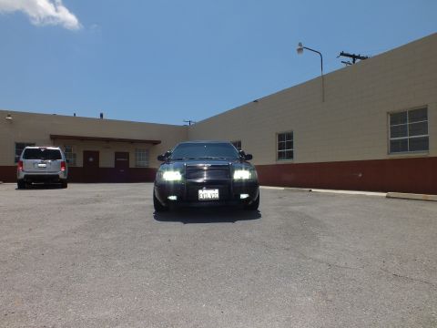 2003 Ford Crown Victoria - Distant front view in parking lot; SUV at left, blacked-out Crown Vic with HIDs lit