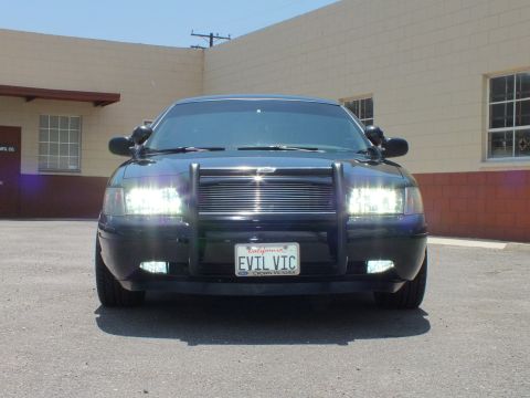 2003 Ford Crown Victoria - Outdoor front shot; EVIL VIC California plate, spotlights, HID headlights against building
