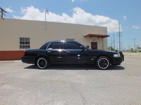 2003 Ford Crown Victoria - Side view, blue sky; lowered black sedan, tinted windows, industrial building backdrop