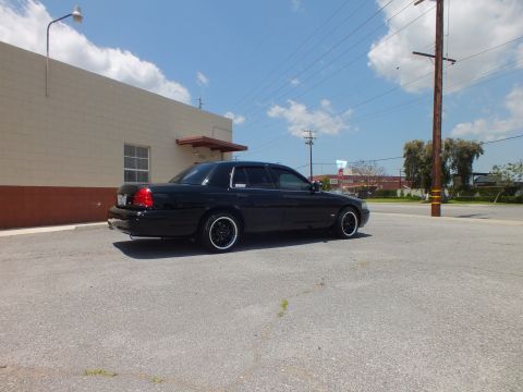 2003 Ford Crown Victoria - Left rear 3/4 in lot; blacked-out sedan, black wheels, power line and sky behind