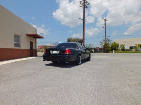 2003 Ford Crown Victoria - Left rear 3/4 from distance; black sedan with spotlights, dual exhaust, lot and pole