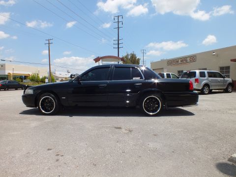 2003 Ford Crown Victoria - Side view of a blacked-out four-door sedan with black multi-spoke wheels in an industrial lot.