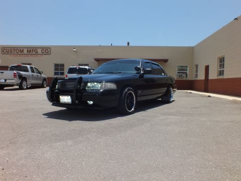 2003 Ford Crown Victoria - Front quarter of a blacked-out sedan with grille guard beside a pickup truck.