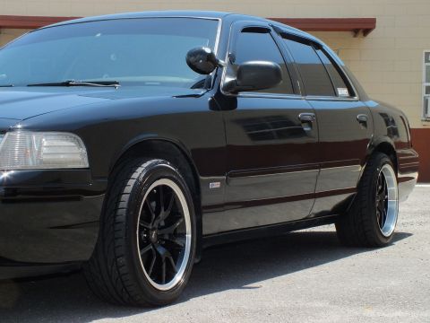 2003 Ford Crown Victoria - Detail of a black sedan's headlight, fender vent and black wheel.