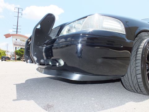 2003 Ford Crown Victoria - Ground-level detail of a black sedan front corner, bumper and tire.