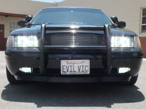 2003 Ford Crown Victoria - Front of a black Crown Victoria with push bar, lit lights and California EVIL VIC plate.
