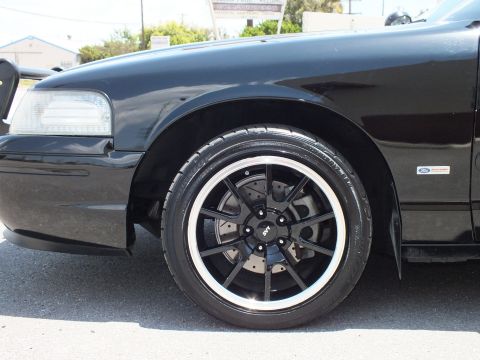 2003 Ford Crown Victoria - Detail of a black sedan front wheel, brake and fender with Ford emblem.