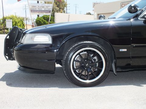 2003 Ford Crown Victoria - Front fender and black wheel of a lowered black sedan in an industrial lot.
