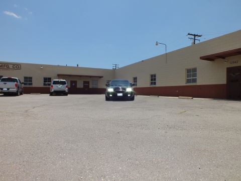 2003 Ford Crown Victoria - Distant head-on view of a black sedan with lit headlights in an industrial parking lot.