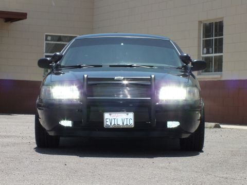 2003 Ford Crown Victoria - Front close-up of a black sedan fitted with a push bumper and EVIL VIC vanity plate.