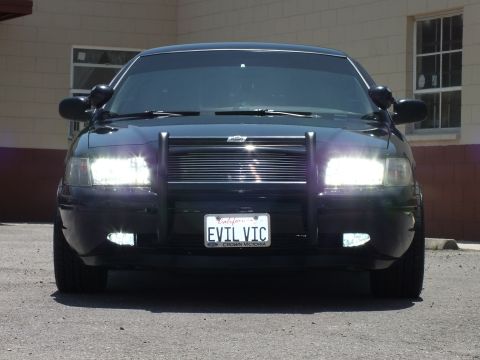 2003 Ford Crown Victoria - Head-on shot of a black sedan with billet grille, brush guard and lit headlights.