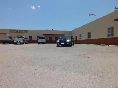 2003 Ford Crown Victoria - Wide lot view: black sedan at center, pickup and SUVs parked by a tan industrial building.