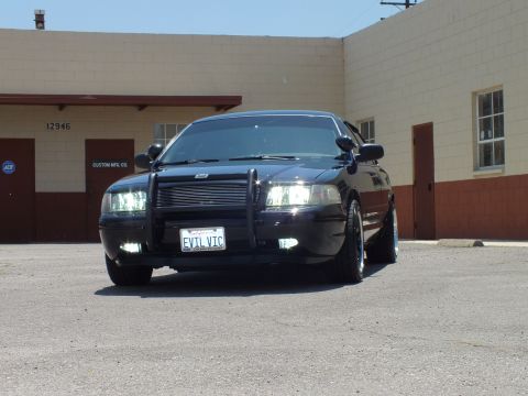 2003 Ford Crown Victoria - Three-quarter front of a lowered black sedan with brush guard parked by warehouse doors.