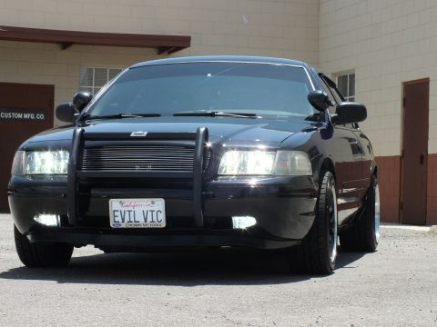 2003 Ford Crown Victoria - Close front-quarter of a black sedan showing chrome grille insert and push bumper.