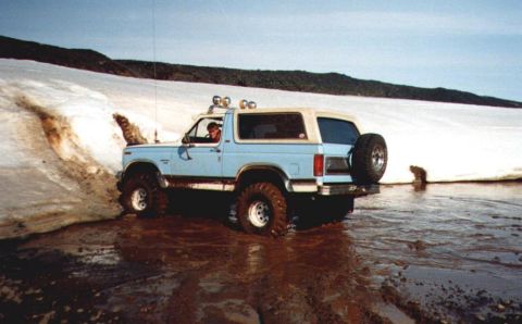 1996 Ford Bronco - Ford Bronco navigates muddy terrain near a snow-covered slope.