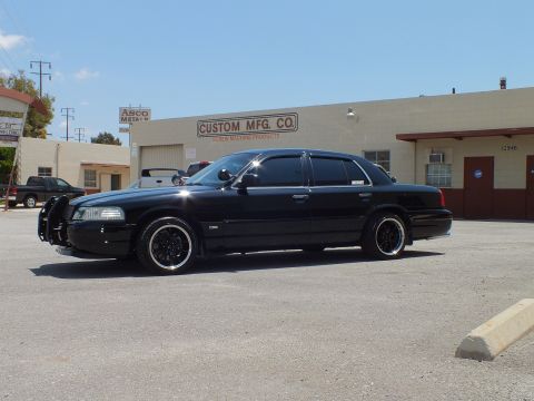 2003 Ford Crown Victoria - Full driver-side view of a lowered black sedan in an industrial lot under blue sky.