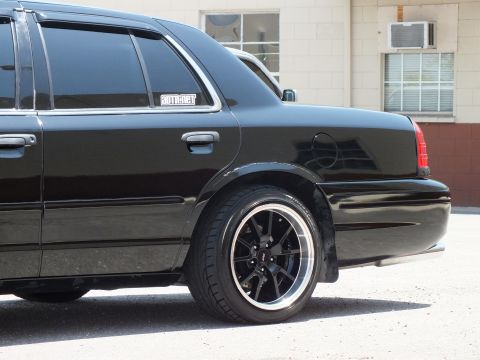 2003 Ford Crown Victoria - Close rear-quarter of a black sedan highlighting the dark polished-lip wheel and taillight.